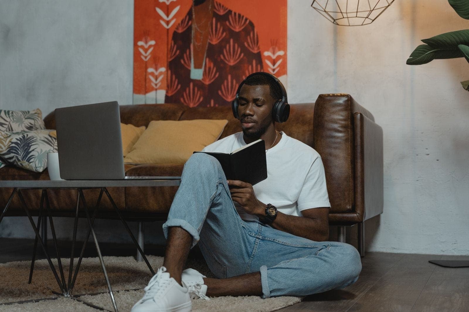 A man wearing headphones and holding a notebook beside his laptop