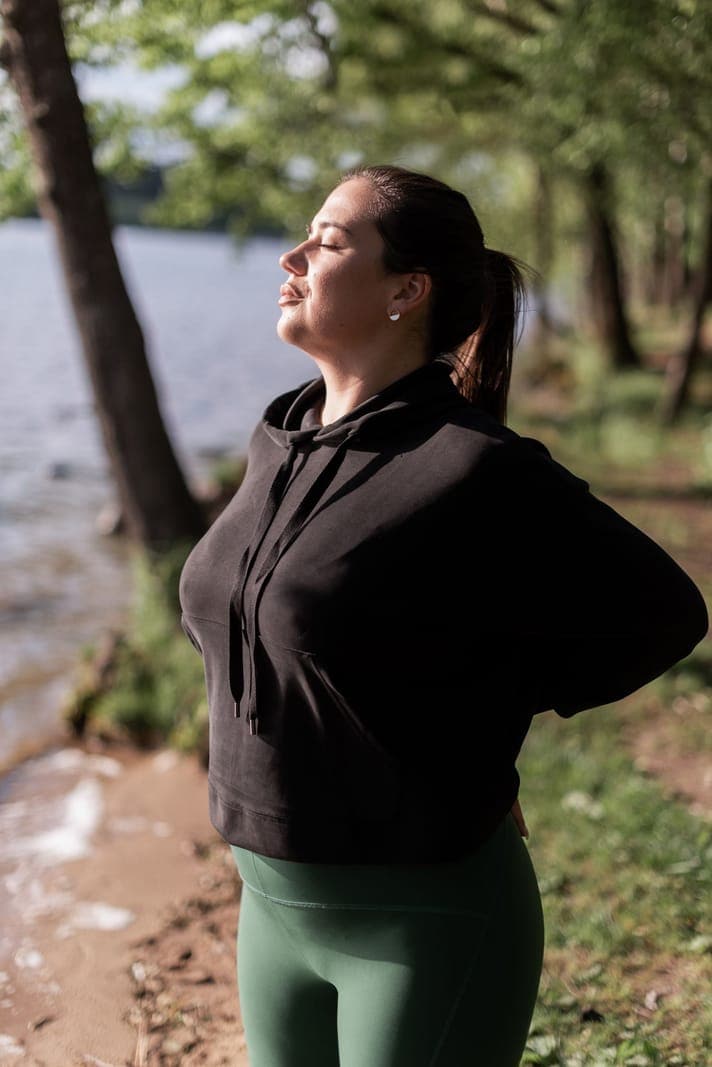 A woman standing outdoors with closed eyes and a relaxed posture