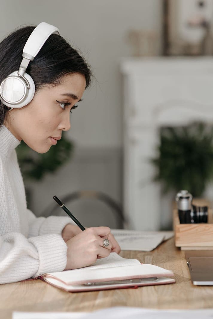 A woman wearing headphones and writing in a notebook
