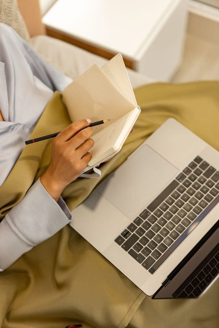 Hands writing in a notebook beside a laptop