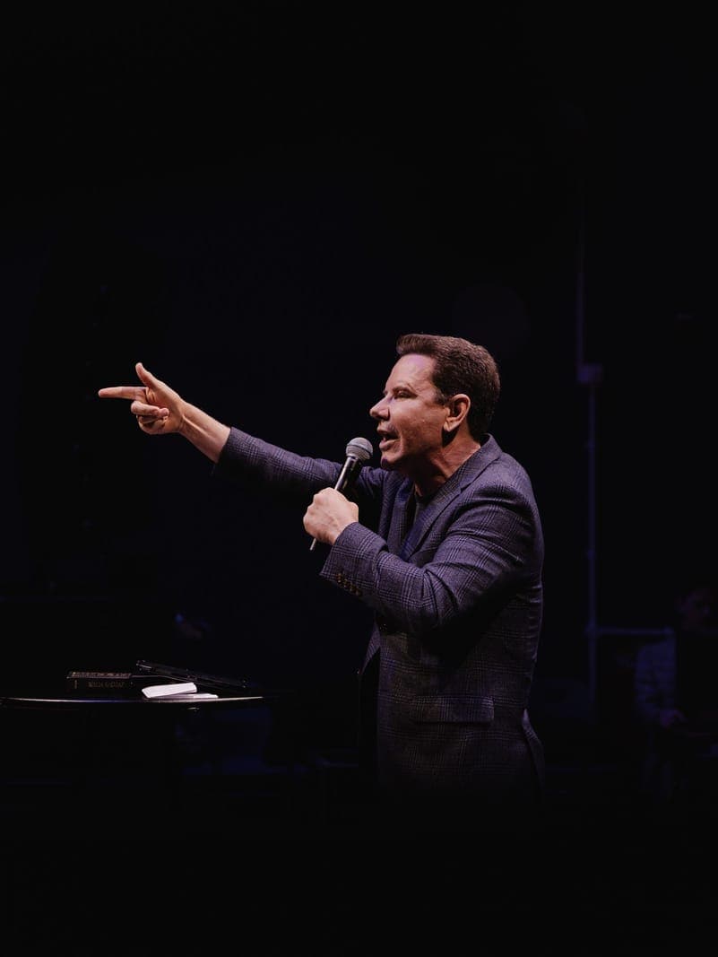 A speaker pointing toward an audience while holding a microphone